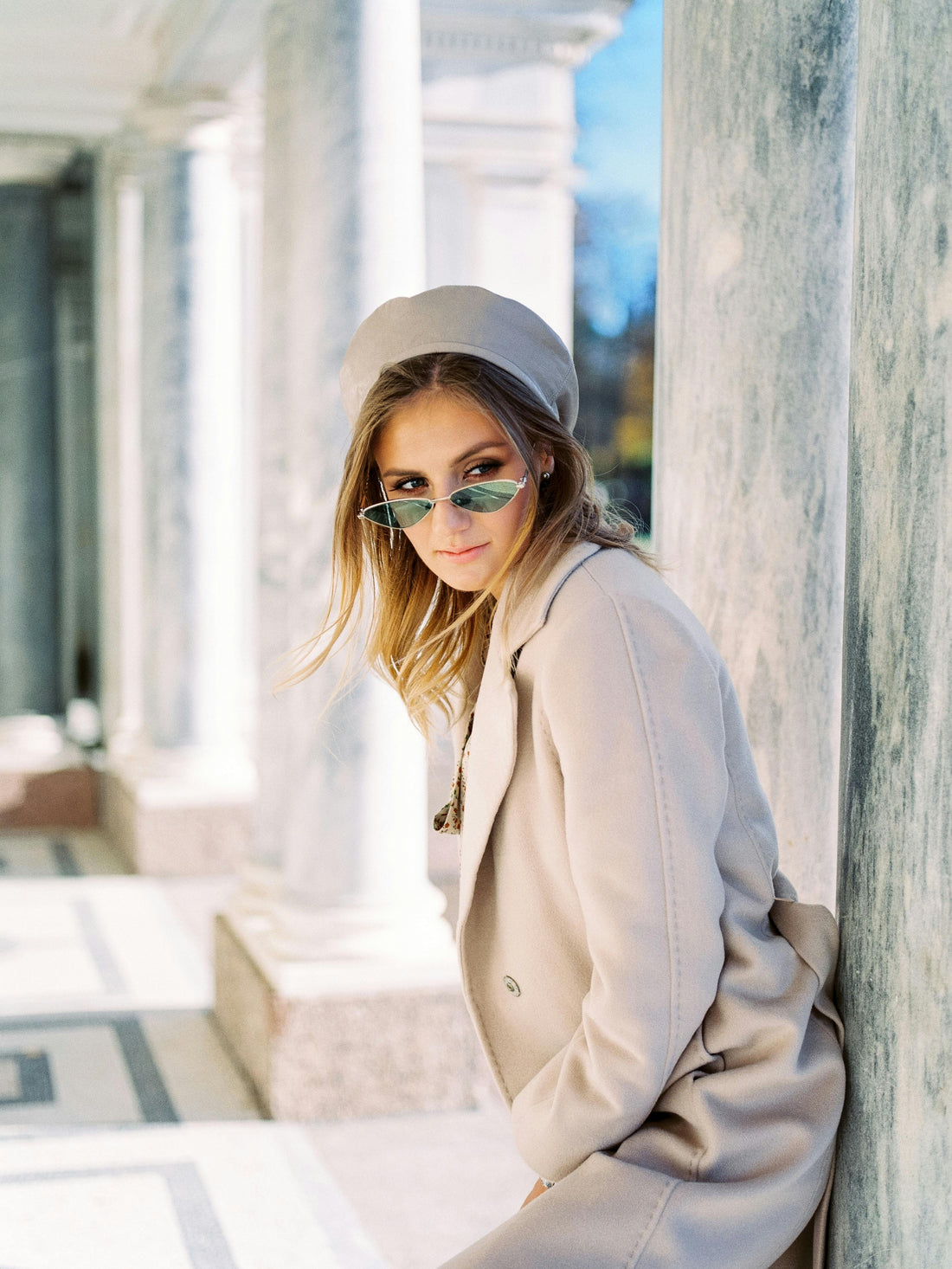 Person with photochromic lens in a light coat and cap leaning against a marble column.